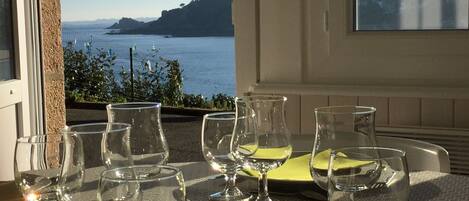 Ein Tisch mit mehreren Weingläsern und einer gelben Serviette, mit Blick auf die Küste, Berge und das Meer.