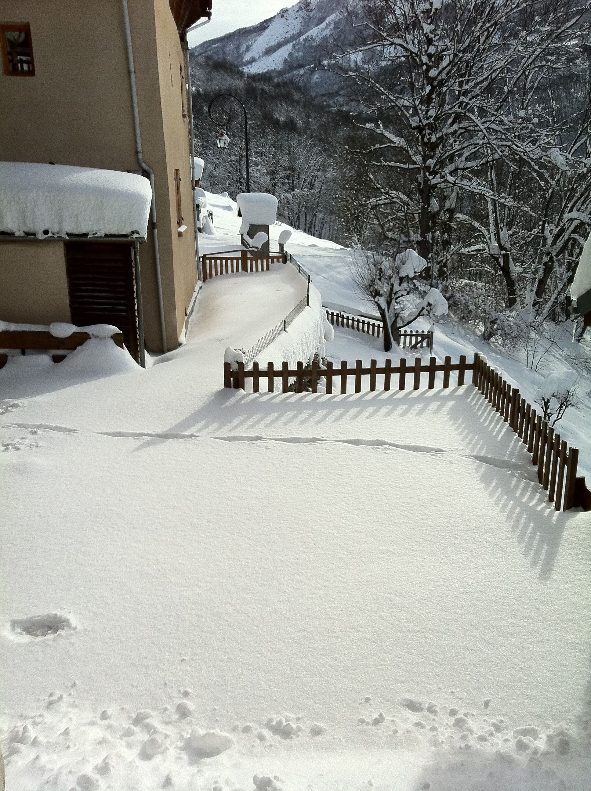 A snow-covered pathway leading to a building with a wooden fence.
