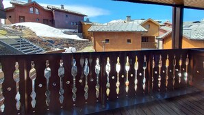 Un balcone in legno con ringhiera decorativa, affacciato su una zona residenziale con case e un pendio innevato.