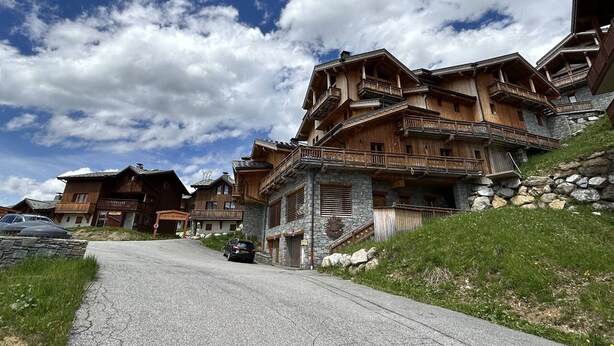 Una fila di edifici in legno tradizionali con balconi, un muro in pietra e una strada pavimentata.