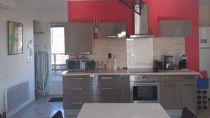 A modern kitchen with grey cabinets, a stainless steel range hood, and a red accent wall. - Private pool for 4 people, air conditioning, landscaped garden and superb view (Lussas)