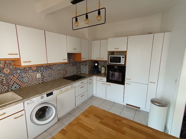 A modern kitchen with white cabinets, a washing machine, a microwave, and a coffee maker.