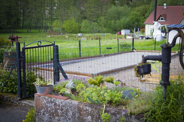 Un espace clos délimité par une clôture, avec un chemin de gravier, un portail en métal et un petit jardin où poussent différentes plantes.