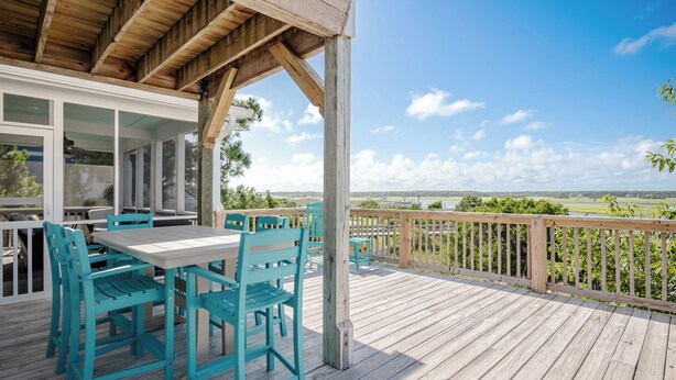 Eine Holzterrasse mit türkisfarbenen Stühlen und einem Tisch mit Blick auf eine malerische Landschaft.