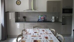 Una cucina moderna con un tavolo da pranzo ricoperto da una tovaglia a tema dessert, un orologio a parete e una macchina da caffè.