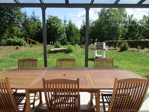 Un patio al aire libre con una mesa y sillas de madera, rodeado de un jardín con diversas plantas y un muro de piedra.
