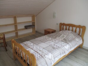 Habitación con una cama individual, cabecera y mesita de noche de madera, estantería empotrada y colcha estampada.