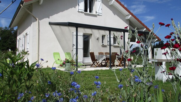 Una casa a due piani con facciata bianca e tetto rosso. È presente un patio con mobili da esterno e un tavolo.