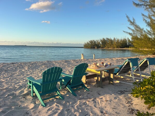 A beach with chairs and a table, a calm sea, and a clear sky.