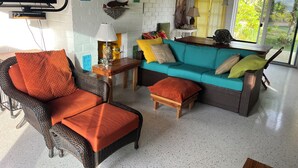 A cozy living room with wicker furniture, a teal sofa, and a flat-screen TV mounted on the wall. - Your Tropical Beach Vacation! (Morgans Bluff)