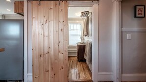 A wooden sliding door leading to a bathroom with a towel rack and a framed picture on the wall. - Vintage Maine & Modern Convenience in Portlands Exclusive East End (Portland)