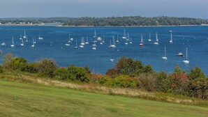 A coastal view with numerous sailboats on a calm sea, surrounded by greenery and a distant shoreline. - Vintage Maine & Modern Convenience in Portlands Exclusive East End (Portland)