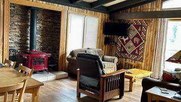 Un salón acogedor con pared de piedra, vigas de madera, estufa roja, sofá de cuero y un tapiz acolchado.