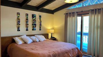 Habitación de hotel con una cama grande, una mesita de noche, una lámpara y vistas al exterior a través de una puerta corredera.