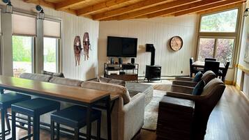 Una sala de estar acogedora con techo de madera, un televisor de pantalla plana, chimenea y un comedor con mesa y sillas.