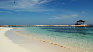 Une plage à l’eau turquoise et limpide, au sable blanc, et agrémentée d’un kiosque en bois installé sur un promontoire rocheux.