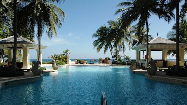 Une piscine bordée de palmiers et agrémentée de gazebos, offrant une vue dégagée sur l’océan.