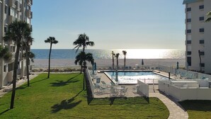 A pool area with a view of the ocean, surrounded by palm trees and a building with balconies. - Beach Front View/access. Updated finishes and open floor plan.   (Fort Myers Beach)