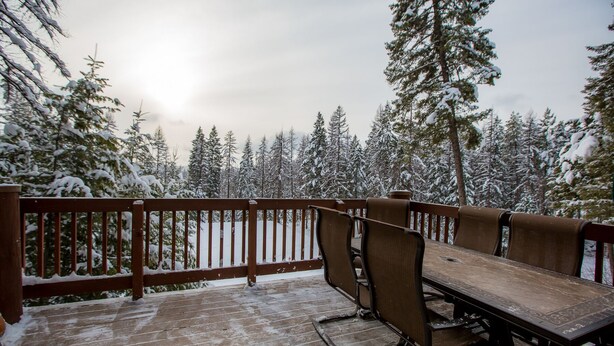 Une terrasse en bois avec une table et des chaises, entourée d’arbres couverts de neige.