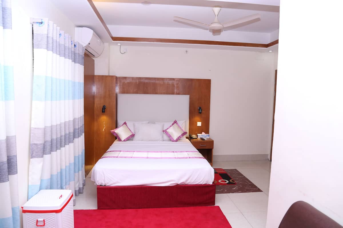 A hotel room with a bed, a nightstand, a red rug, and a ceiling fan.