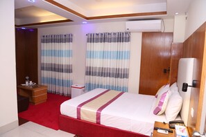 A hotel room with a bed, a desk with a chair, a small table, and a red carpet. - Platinum Hotel Ltd (Dhaka)