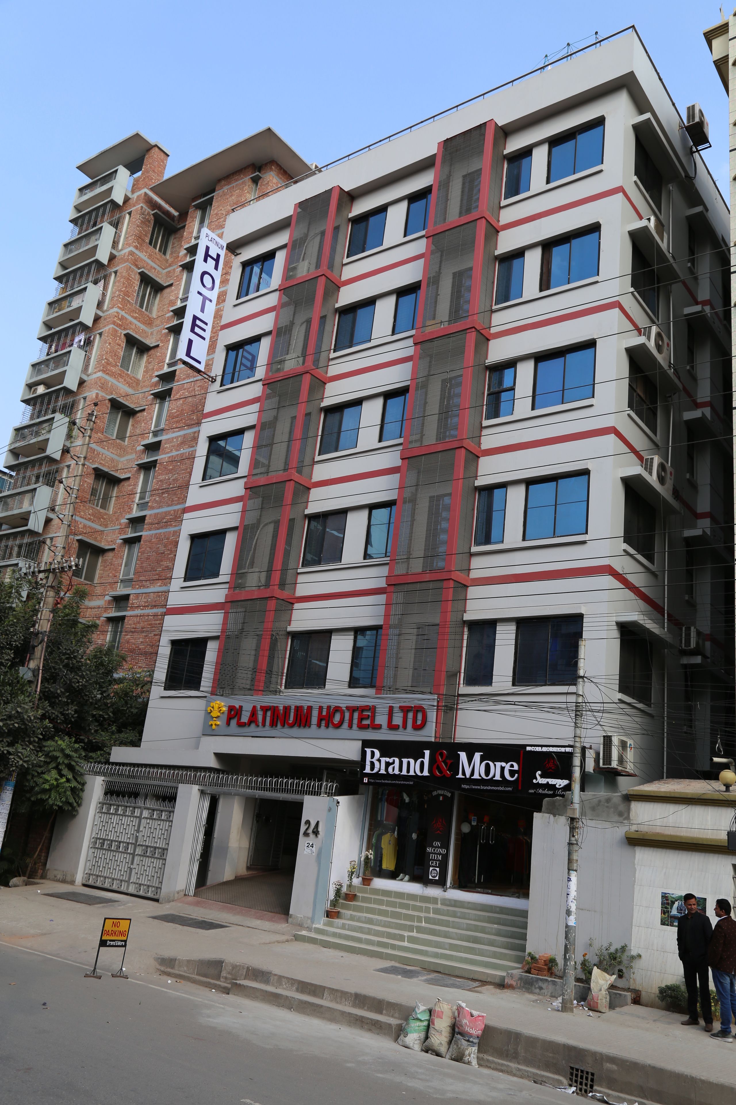A multi-story hotel with a prominent 'Platinum Hotel Ltd' sign, a 'Brand & More' store on the ground floor, and a 'No Parking' sign in front.