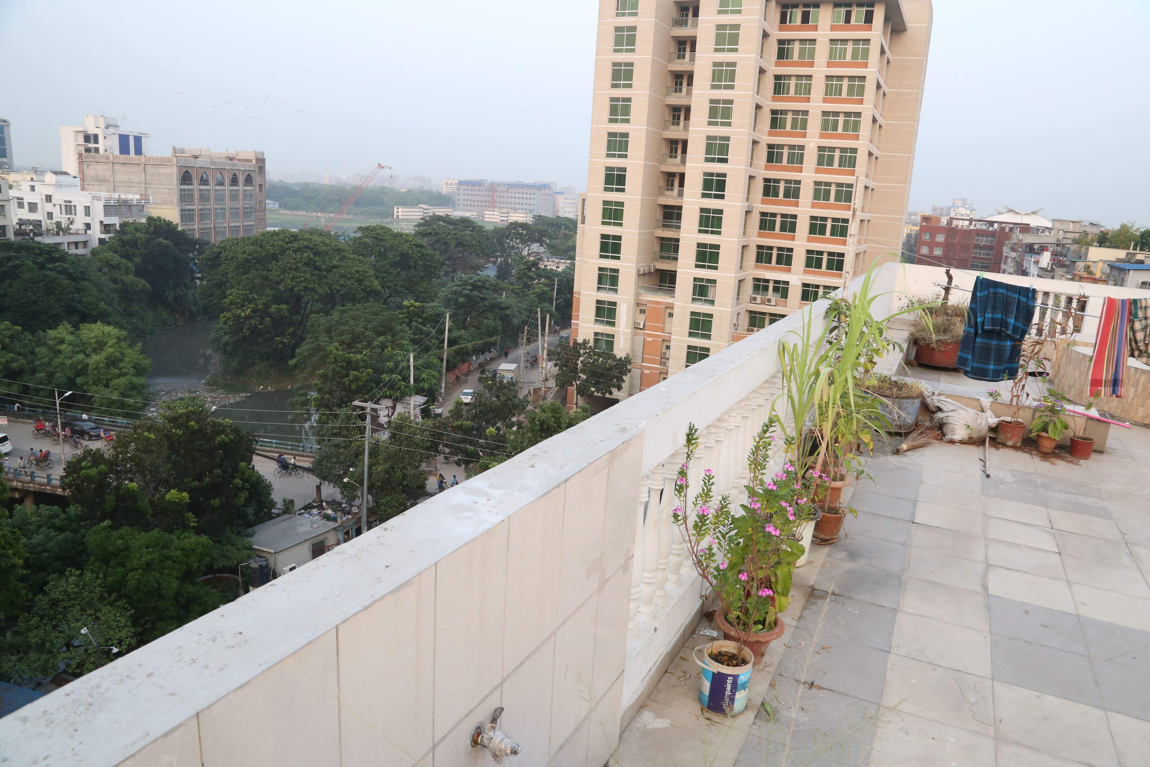 A high-rise building with multiple floors, a balcony with potted plants, and a view of a busy street below.