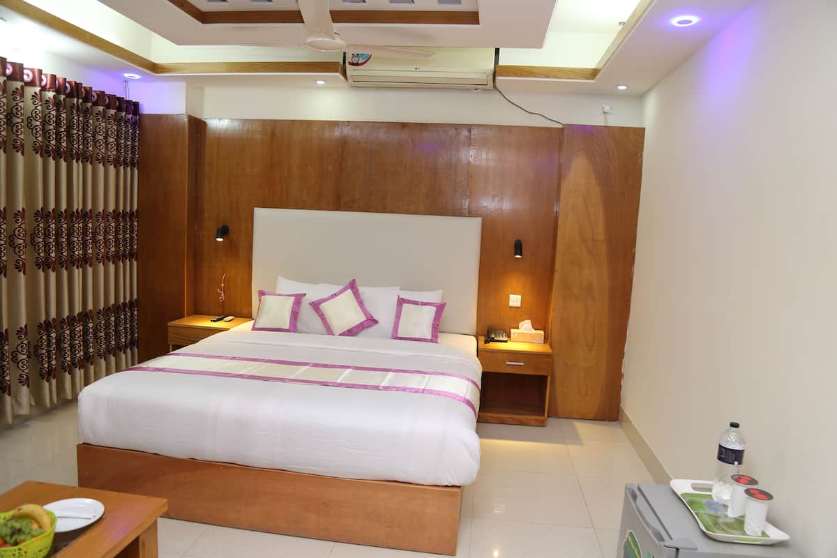 A modern hotel room with a large bed, wooden headboard, bedside tables with lamps, and a small table with a bowl and plates.
