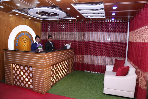 Una zona de recepción con un mostrador de madera, un sofá blanco con cojines rojos y cortinas rojas.