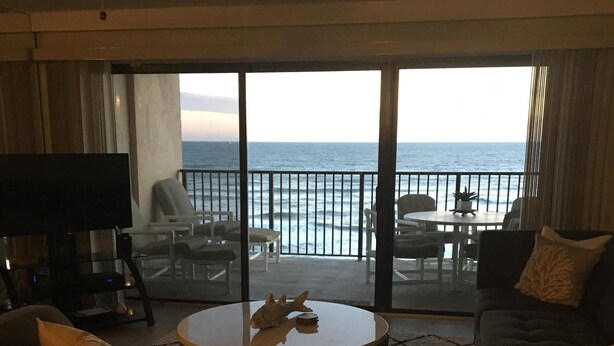Ein Wohnzimmer mit großem Fenster zum Meer, einem Deckenventilator und einem Flachbildfernseher.