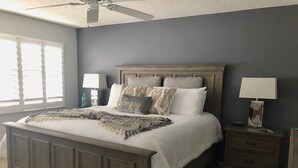Ein Schlafzimmer mit einem großen Bett, zwei Nachttischen, einem Deckenventilator und einem Fenster mit Jalousien.
