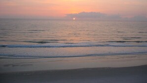 Ein Strand mit sanften Wellen und einem Sonnenuntergang in der Ferne.