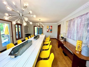 Uma sala de jantar com uma mesa comprida, cadeiras amarelas e um lustre moderno.