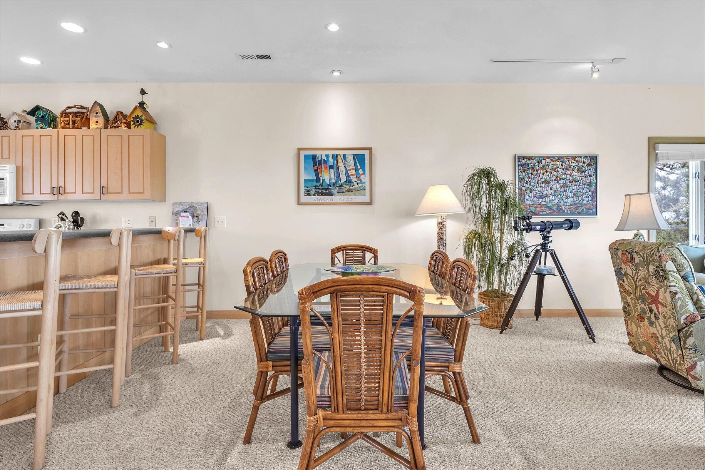 A dining area with a glass-top table, wicker chairs, a buffet counter, and wall-mounted artwork.