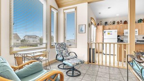 Un'ampia zona giorno con mobili in vimini, vista attraverso ampie finestre e una cucina con pensili in legno.