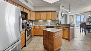 A modern kitchen with wooden cabinets, stainless steel appliances, and a large island. - White Caps 1206 by Liquid Life (Orange Beach)