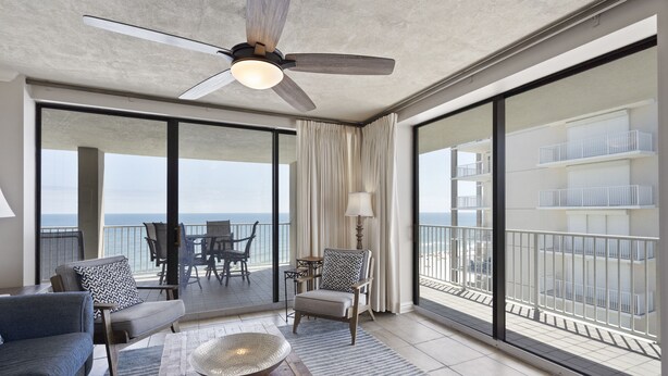 A spacious balcony with a ceiling fan, a wooden coffee table, and seating. - White Caps 1206 by Liquid Life (Orange Beach)