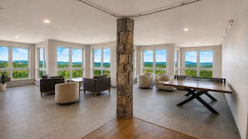 A spacious room with a ping pong table, multiple seating areas, and large windows offering a view of greenery.