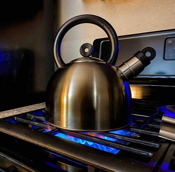 A stainless steel kettle on a gas stove with blue flames.
