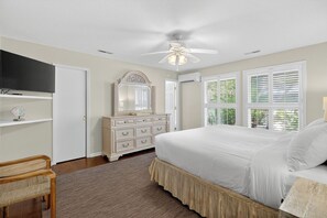 A bedroom with a bed, dresser, mirror, ceiling fan, and large windows.