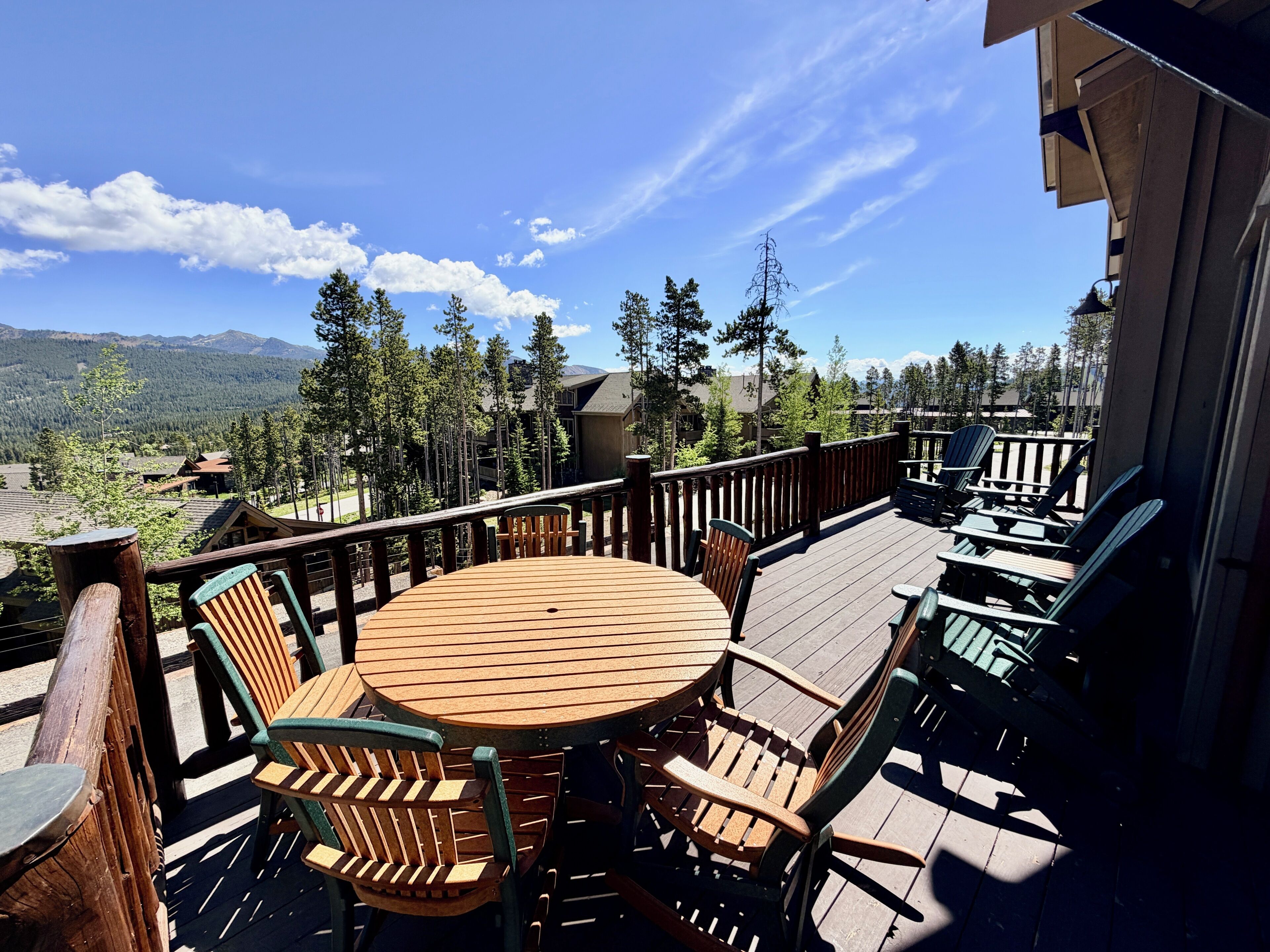 A wooden deck with a round table and chairs, overlooking a mountainous landscape.