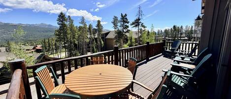 A wooden deck with a round table and chairs, overlooking a mountainous landscape.