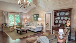Un soggiorno accogliente con soffitto alto, pareti in legno, un lampadario e una collezione di piatti decorativi.