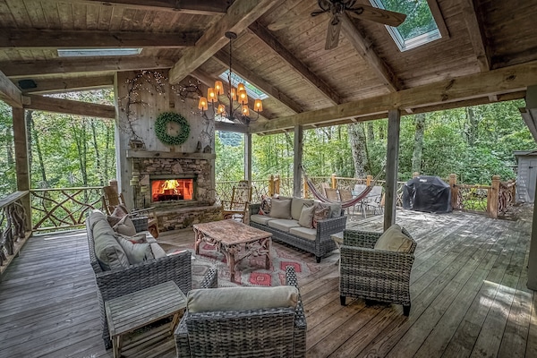 The deck features a wood-burning fireplace and is surrounded by a lush forest