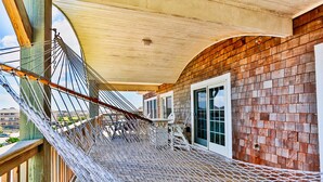 A hammock bridge with a wooden deck, a covered area with a roof, and a brick wall with a window.
