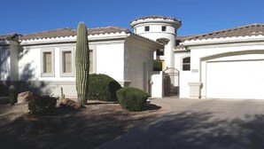 Une maison blanche avec une tour ronde, un garage et un cactus dans le jardin.