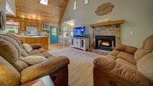 A cozy living room with a fireplace, a kitchen with wooden cabinets, and a dining area with a TV.