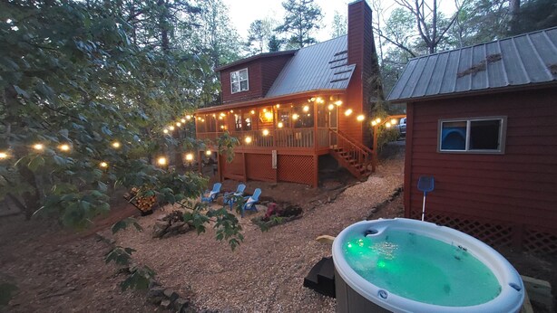 A wooden deck with string lights, a hot tub, and a small building with a window.