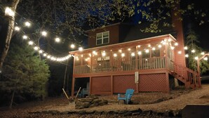 A two-story wooden cabin with a balcony, string lights, and outdoor seating.