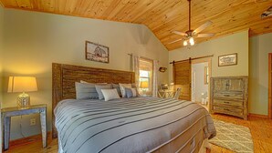 A bedroom with a large bed, wooden ceiling, and a ceiling fan.